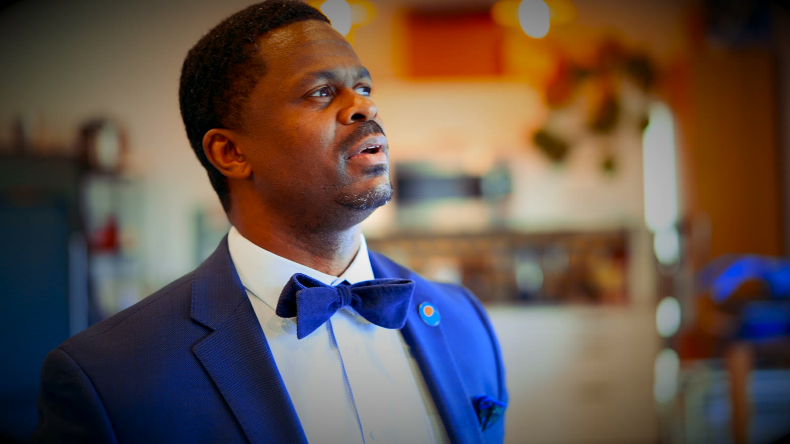 Dennis Williams Jr in a blue suit and bow tie, mid-conversation in a Seattle coffee shop